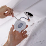 An electrician installs a recessed light into a drywall tile.