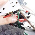 An electrician is reattaching wires to the appropriate connection points in an outlet.