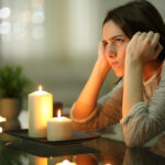 A tenant sits by candlelight, frustrated because the power is out in their apartment.